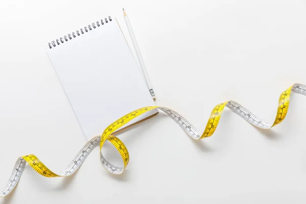 Vista dall'alto del nastro di misurazione, notebook bianco con matita su sfondo bianco — Foto stock