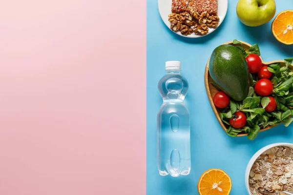 Vista superior de la botella con agua y alimentos dietéticos sobre fondo azul y rosa - foto de stock