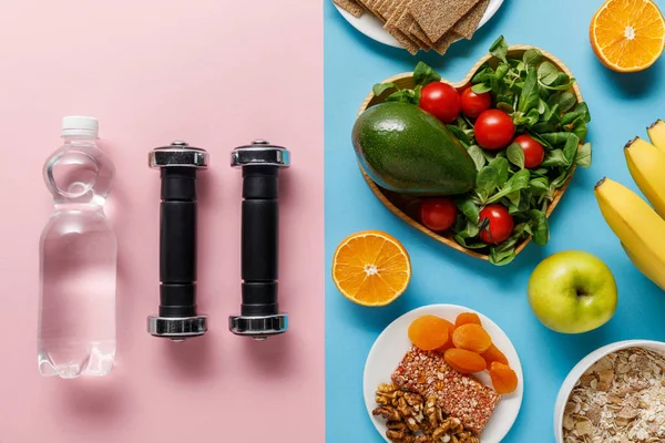 Vista dall'alto del cibo dieta vicino a manubri e acqua su sfondo blu e rosa — Foto stock