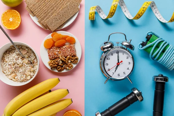 Vue de dessus des fruits frais, pain croustillant et céréales pour petit déjeuner sur rose et haltères, réveil, corde à sauter et ruban à mesurer sur fond bleu — Photo de stock