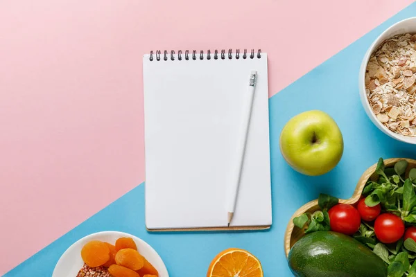 Top view of empty notebook and pencil with delicious diet food on blue and pink background — Stock Photo