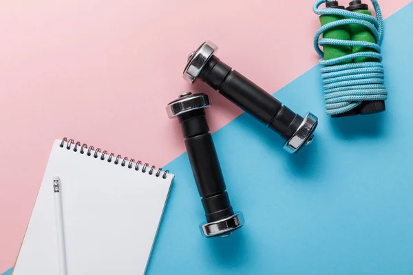 Vista dall'alto di corda da salto, manubri e notebook su sfondo blu e rosa — Foto stock