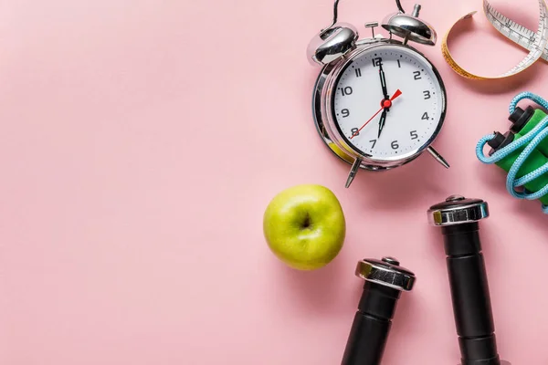 Vista superior de manzana verde fresca, mancuernas, cinta métrica, saltar la cuerda y el reloj despertador sobre fondo rosa con espacio para copiar - foto de stock