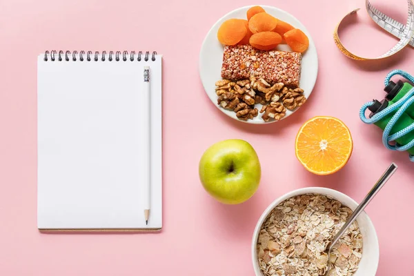 Vista superior de alimentos dietéticos frescos, cinta métrica, saltar la cuerda y el cuaderno en blanco sobre fondo rosa con espacio para copiar - foto de stock