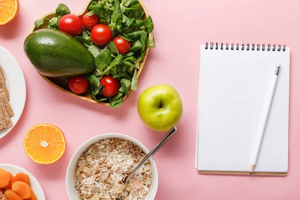 Top view of fresh diet food and blank notebook on pink background — Stock Photo