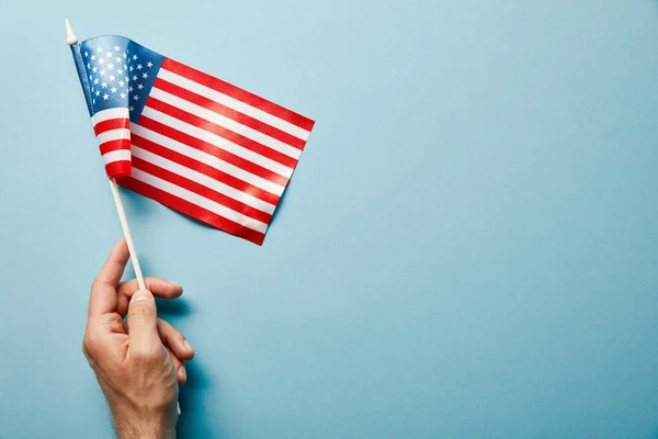 Vue recadrée de l'homme tenant drapeau américain sur bâton sur fond bleu avec espace de copie — Photo de stock