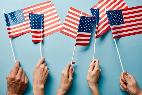 Vista parcial de personas sosteniendo banderas americanas sobre fondo azul - foto de stock