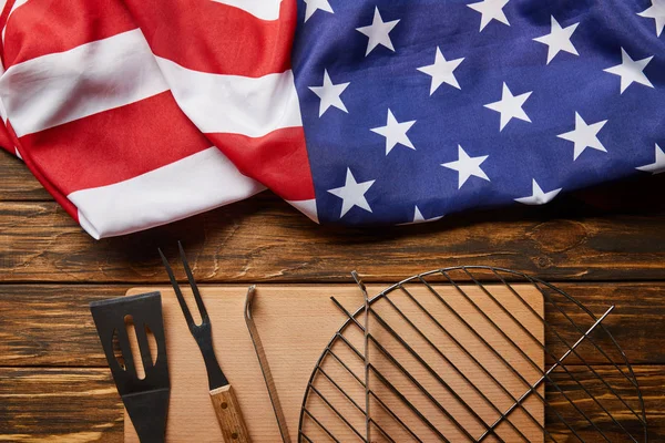 Vista superior de la bandera americana arrugada y el equipo de barbacoa en la mesa rústica de madera - foto de stock