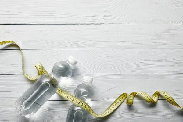 Top view of bottles with water and yellow measuring tape on wooden white background with copy space — Stock Photo