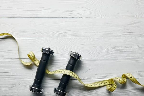 Top view of measuring tape and dumbbells on wooden white background with copy space — Stock Photo