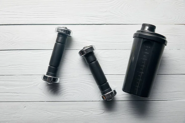 Top view of black shaker cup and dumbbells on wooden white background — Stock Photo