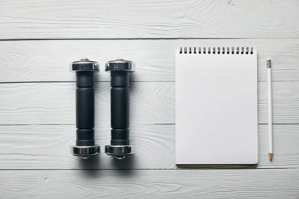 Tendido plano con pesas, cuaderno en blanco con espacio para copiar y lápiz sobre fondo blanco de madera - foto de stock