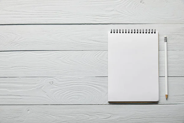 Flat lay com notebook em branco com espaço de cópia e lápis sobre fundo branco de madeira — Fotografia de Stock