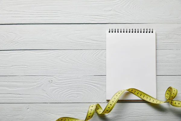 Top view of measuring tape and blank notebook with copy space on wooden white background — Stock Photo