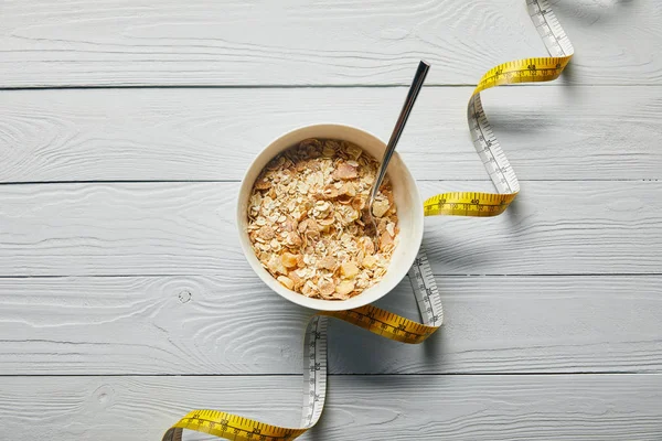 Top view of measuring tape, spoon and breakfast cereal in bowl on wooden white background — Stock Photo