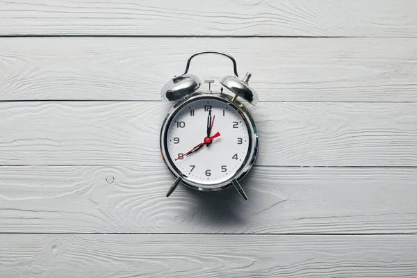 Vista superior del reloj despertador plateado sobre fondo blanco de madera - foto de stock