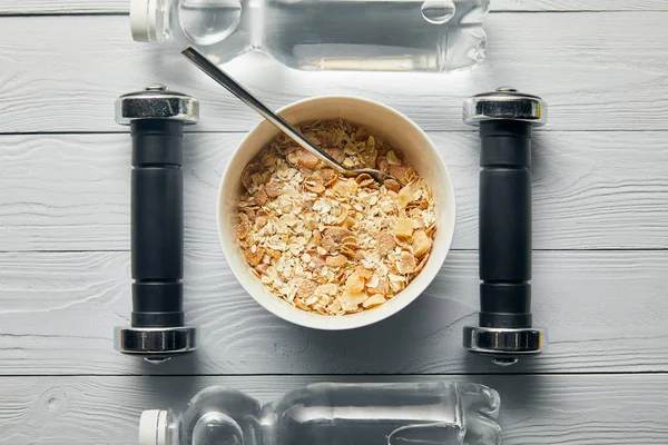 Plano con cereales para el desayuno en tazón, botellas con agua, pesas sobre fondo blanco de madera - foto de stock