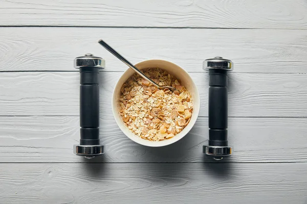 Plano con cereales para el desayuno en tazón y pesas sobre fondo blanco de madera - foto de stock