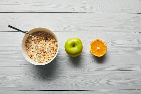 Plano con cereales para el desayuno en tazón, manzana, naranja sobre fondo blanco de madera - foto de stock