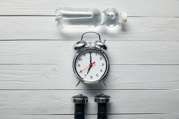 Flat lay with alarm clock, bottle of water and dumbbells on wooden white background — Stock Photo