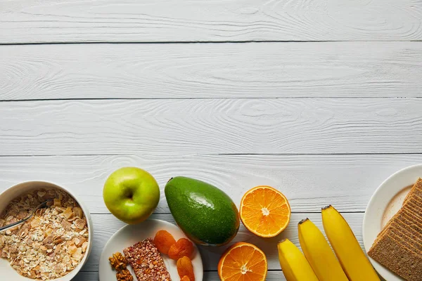 Ansicht von Frühstückszerealien in Schüssel, Nüssen, Knäckebrot und reifen Früchten auf weißem Holzhintergrund mit Kopierraum — Stockfoto