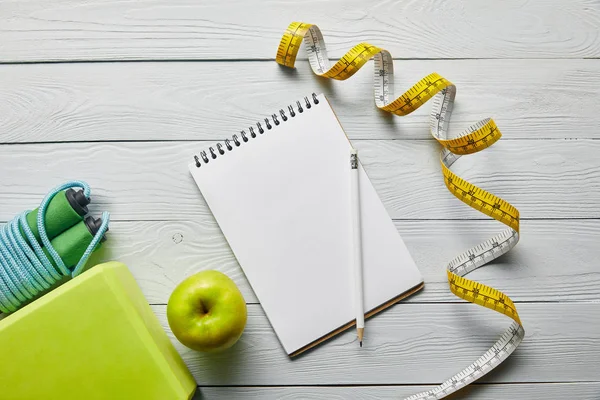 Maßband, grüne Schachtel und Apfel, Springseil, Notizbuch und Bleistift auf weißem Holzgrund — Stockfoto