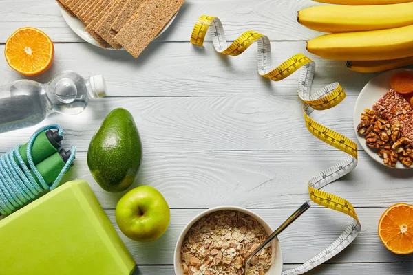 Top view of diet food near measuring tape and sport equipment on wooden white background with copy space — Stock Photo