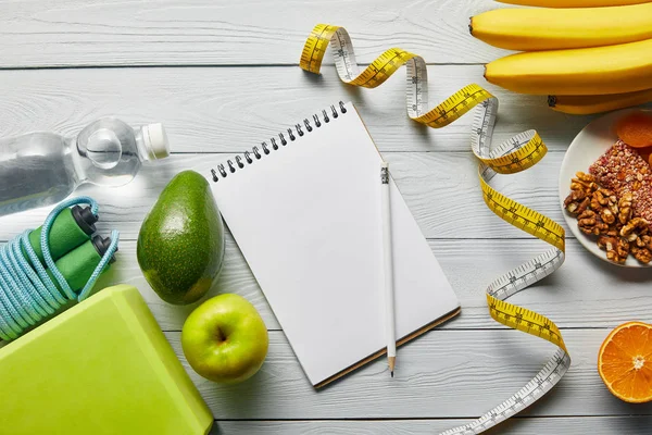 Top view of diet food near measuring tape, notebook and sport equipment on wooden white background — Stock Photo