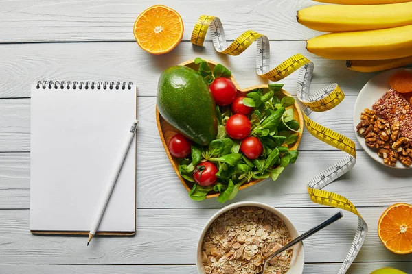 Vista superior de fita métrica, notebook em branco e cereais, frutas e legumes em fundo branco de madeira — Fotografia de Stock