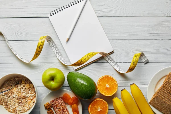 Top view of measuring tape, diet food and blank notebook on wooden white background — Stock Photo