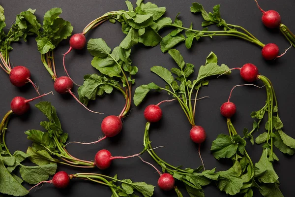 Top view of whole tasty radish with green leaves on black background — Stock Photo