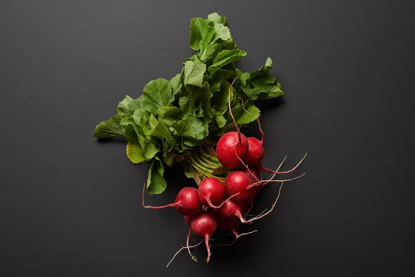 Top view of raw nutritious tasty radish with green leaves on black background — Stock Photo