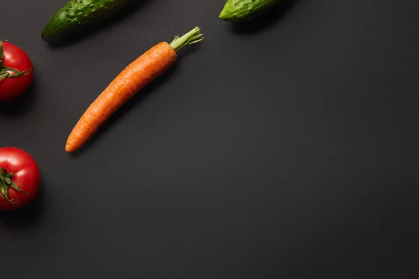 Vue du dessus des carottes crues, des concombres et des tomates sur fond noir avec espace de copie — Photo de stock