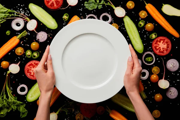 Abgeschnittene Ansicht der Frau mit leeren runden Teller auf Gemüsemuster Hintergrund isoliert auf schwarz — Stockfoto