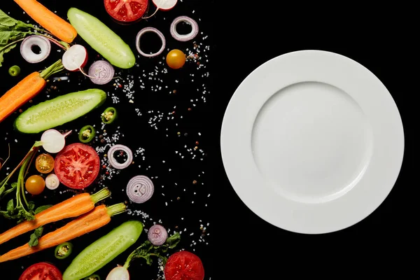 Vista superior de la placa redonda vacía cerca de rebanadas de verduras aisladas en negro - foto de stock