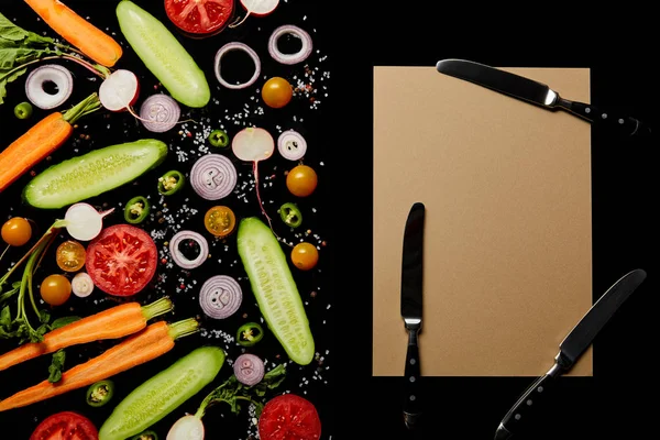 Vue de dessus des tranches de légumes frais avec du sel près du papier blanc et des couteaux isolés sur noir — Photo de stock