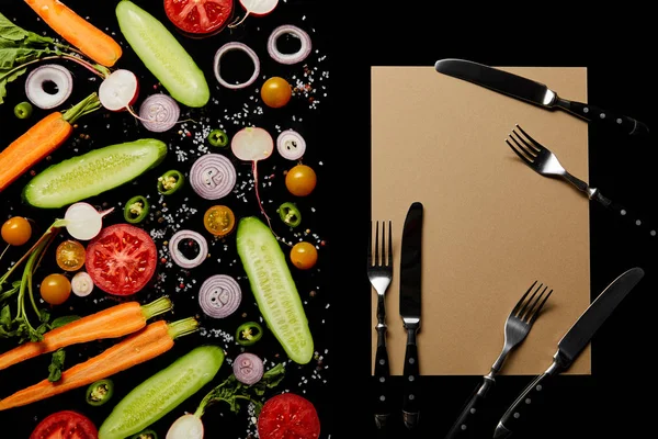 Vista dall'alto di fette di verdure fresche con sale vicino carta bianca con coltelli e forchette isolate su nero — Foto stock
