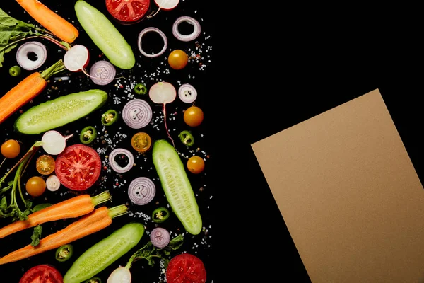 Вид сверху на свежие овощные ломтики с солью рядом с бумагой коричневый пустой изолирован на черном с места для копирования — стоковое фото