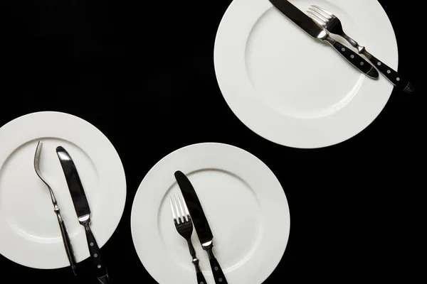 Top view of white round plates with cutlery isolated on black — Stock Photo