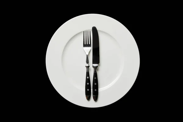 Top view of white round plate with knife and fork isolated on black — Stock Photo