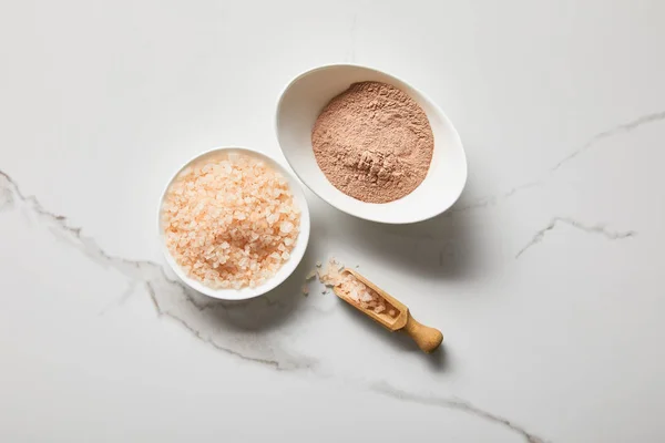 Top view of clay powder and sea salt in bowls on marble table near wooden spatula — Stock Photo