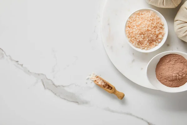 Top view of clay powder and sea salt in white bowls on marble table near wooden spatula — Stock Photo