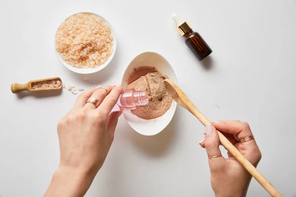 Vue recadrée de la femme ajoutant du liquide à la poudre d'argile tout en préparant des cosmétiques biologiques — Photo de stock