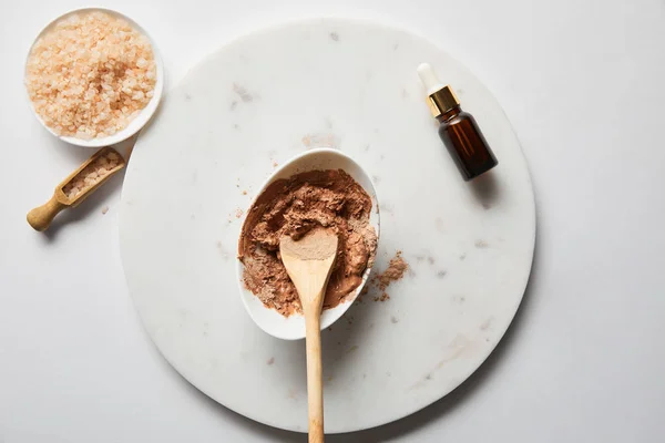 Vista superior de arcilla en tazón con cuchara de madera cerca de sal marina y aceite sobre mesa de mármol — Stock Photo