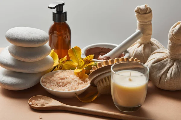 Spa cosmetics, stones, massage brush, candle and yellow flowers on beige surface isolated on grey — Stock Photo