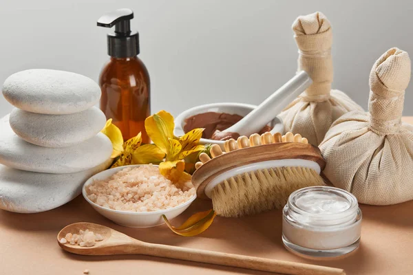 Vari cosmetici spa, pietre, spazzola per massaggi, candele e fiori gialli su superficie beige isolata su grigio — Foto stock
