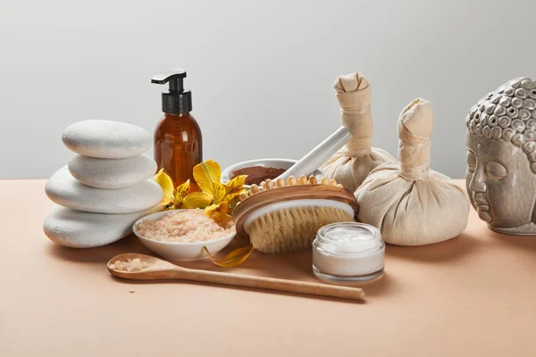 Cosmétiques spa, pierres, brosse de massage, bougie, figurine de Bouddha et fleurs jaunes sur la surface beige isolé sur gris — Photo de stock