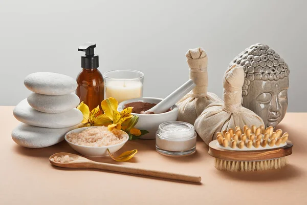 Spa cosmetici, pietre, spazzola da massaggio, candela, Buddha figurina su superficie beige isolato su grigio — Foto stock