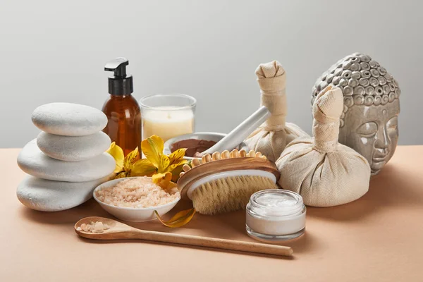 Cosmétiques spa, pierres, brosse de massage, bougie, fleurs jaunes, figurine de Bouddha sur la surface beige isolé sur gris — Photo de stock