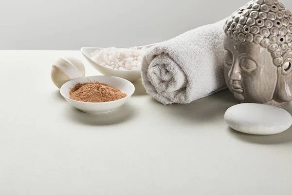 Sea salt and clay powder in bowls, cotton towel, stone, bath bomb and Buddha figurine on white table isolated on grey — Stock Photo